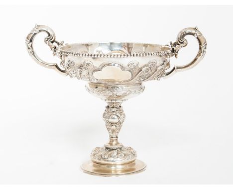 An Edwardian silver two handled cup on stand, the ogee bowl with beaded rim above S scroll floral chased sections and vacant 