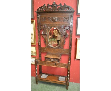 A late Victorian carved oak hall stand, heraldic pediment with stylized dragons, oval mirror flanked by winged dragons and co