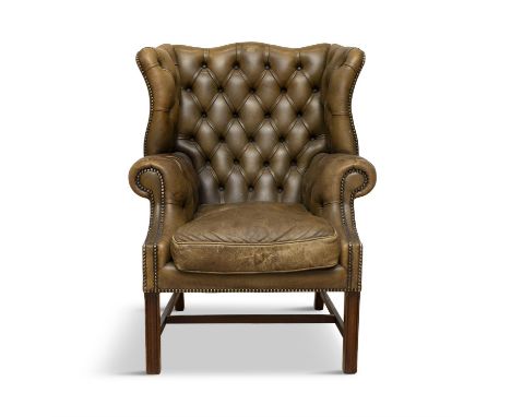 A MAHOGANY FRAMED WINGBACK ARMCHAIRupholstered in green button back leather, with brass studding, loose seat cushion, raised 