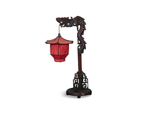AN ORIENTAL FRUITWOOD TABLE LAMP,in the form of a stylised dragon, raised above a circular base with red silk shade, electrif