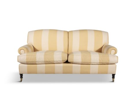 AN UPHOLSTERED HOWARD STYLE SOFAcovered in a yellow and beige striped fabric, with loose seat cushions, supported on short tu