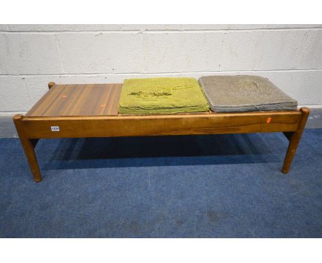 A 1960'S TEAK BENCH/COFFEE TABLE, the triple reversable inserts with cushion seat pads upholstered in red, green and grey, le