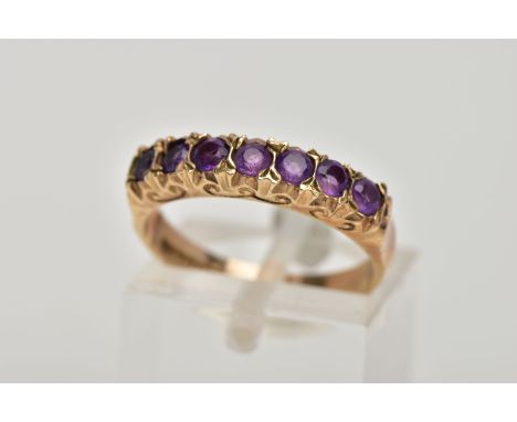 A 9CT GOLD AMETHYST HALF ETERNITY RING, designed with a row of seven circular cut amethysts, scroll detailed gallery, plain p