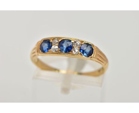 A YELLOW METAL SAPPHIRE AND DIAMOND RING, designed with a row of three circular cut blue sapphires, interspaced with four sma