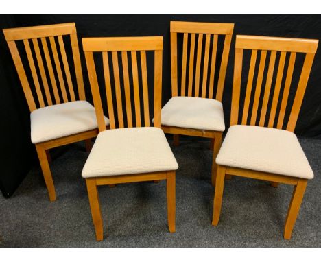 A set of four modern light wood dining chairs, cream upholstered seats. 