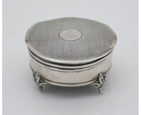 A sterling silver engine decorated round trinket box with red velvet interior, circular cartouche to the lid and sitting on f