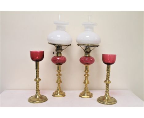 Pair of small oil lamps, the cranberry glass reservoirs on brass candlestick columns, with opaque white glass shades, each 51