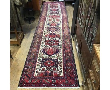 A Caucasian hand knotted wool runner, the central panel with alternating geometric medallions enclosed within  a multiple flo