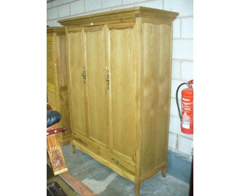 A Light oak French style triple wardrobe with a cavetto cornice above three panelled cupboard doors , two drawers and curvili