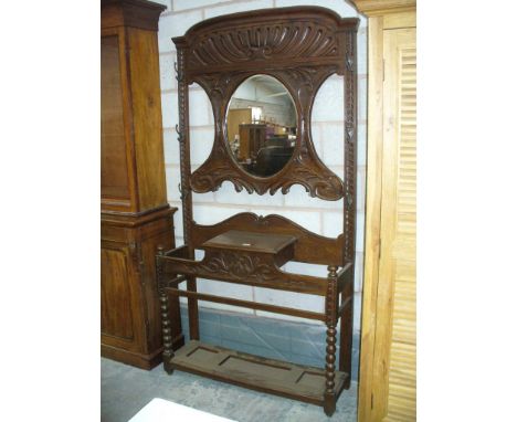 A Late Victorian carved oak hall stand
The scrolling leaf carved back centred with an oval mirror above a hinged glove box an