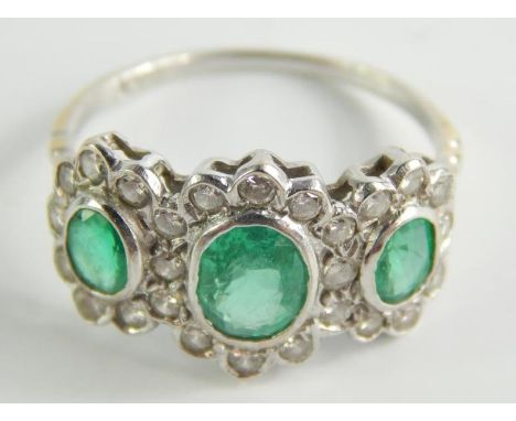 An emerald and diamond ring, with three oval emeralds, surrounded by tiny diamonds, in a white metal setting, on yellow metal