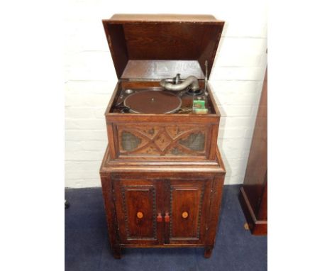 An HMV oak cased cabinet gramophone, the lift lid above a record player set sound box, over a pair of paterae inlaid doors, r