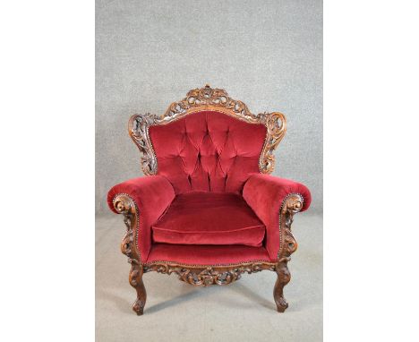 A 20th century continental walnut armchair, upholstered in red velour, with a button back, the frame profusely carved and pie