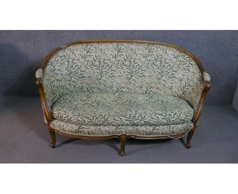 A French Louis XVI style walnut framed canape sofa, with a curved back, upholstered in a printed foliate fabric, with scrolli