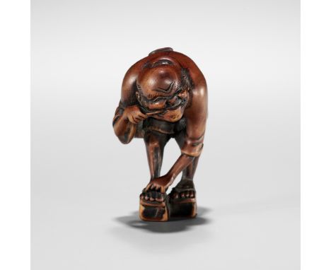 AN EDO SCHOOL WOOD NETSUKE OF A FARMER TYING HIS GETA AND CLEANING HIS TEETHUnsigned Japan, Edo (Tokyo), early to mid-19th ce