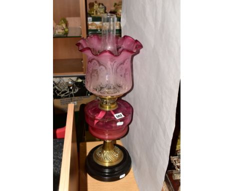 A LATE VICTORIAN CRANBERRY GLASS AND BRASS OIL LAMP, the wavy rimmed shade acid etched with floral designs, cranberry glass r