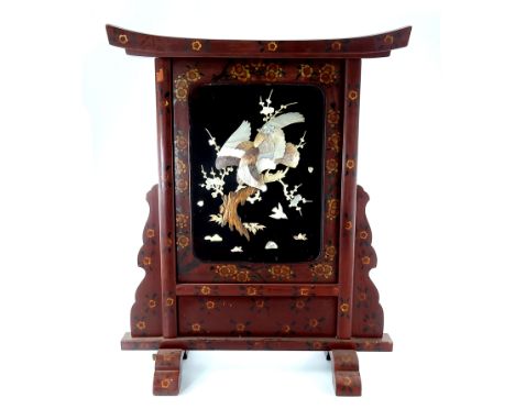 A Japanese lacquer and shibayama fire screen, Meiji, traditional gate form, the central panel applied and carved in high reli