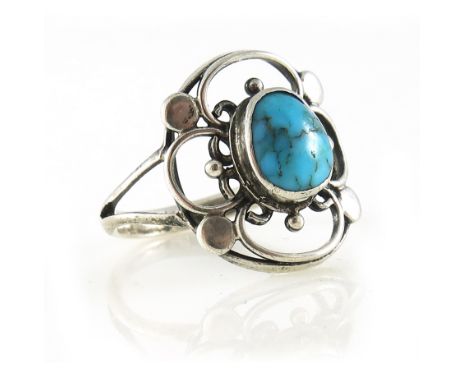 An Arts and Crafts silver turquoise ring, designed as a turquoise cabochon, within an open wire quatrefoil rosette, with disc