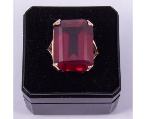 A large dress ring with a rectangular step cut synthetic ruby (corundum), four claw set in an all rose coloured metal mount, 