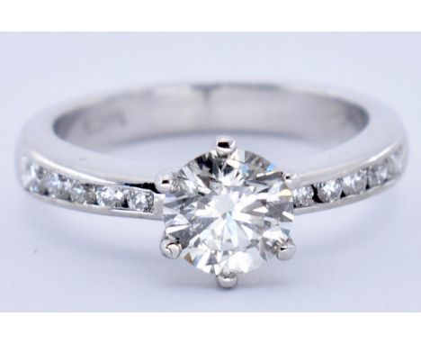 An 18ct white gold and diamond solitaire ring. The ring set with a round brilliant cut diamond having channel set diamond sho