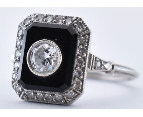 A platinum onyx and diamond panel ring. The ring set with a central round brilliant cut diamond within an octagon cut onyx pl