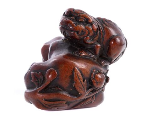 A carved boxwood netsuke,Edo period, 18th century, Japanese, in the form of a Shishi crouching on a rock with a flowering peo