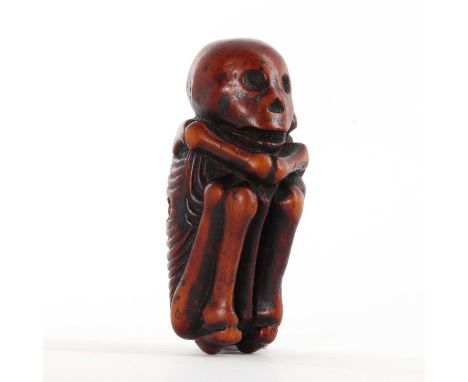 A Japanese carved boxwood netsuke depicting a skeleton,Edo period, 19th century, the skeleton in a foetal position for transi