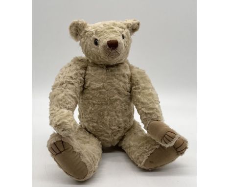 A Steiff style teddy bear with glass eyes, plush fur, fully jointed limbs and stitched nose and claw detail. There is a small