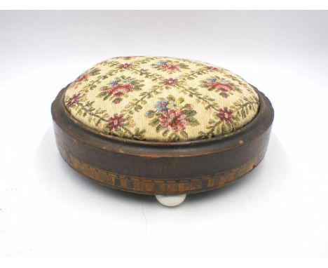An inlaid upholstered footstool with ceramic feet.