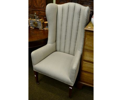 An upholstered high back wing armchair on tapering square support 