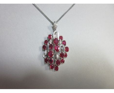 A ruby and diamond pendant cased by Asprey, of open abstract design and oval domed form, and set with eighteen oval cut rubie