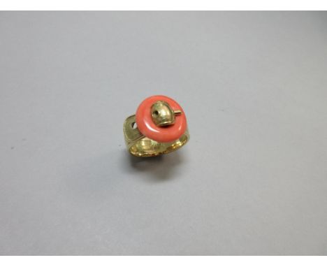 A buckle ring by Piaget of 18ct gold and coral, the uniform broad band textured to the front and with a realistically modelle