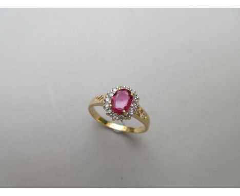 A ruby and diamond cluster ring, the oval cut ruby claw set in a border of small round brilliant cut diamonds, to pierced sho