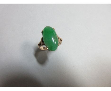 A jadeite jade ring, the oval cabochon mid-green jade four claw set to looped and beaded shoulders and a plain tapered shank,