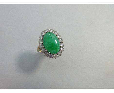 A jade and diamond cluster ring, the oval cabochon jadeite jade of emerald green hue, claw set to a border of sixteen round b