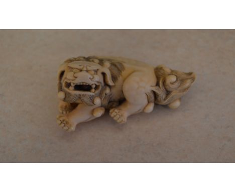 An ornately carved ivory netsuke of a seated Shishi / Guardian Lion with moveable ball in open mouth