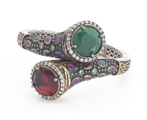 A continental past set hinged bangle, of crossover design set with red, green synthetic gem stones with cast decoration to th