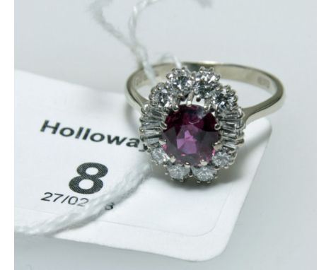 A ruby and diamond cluster ring, the oval cut ruby in raised claw mount, within a border of brilliant and trapeze cut diamond