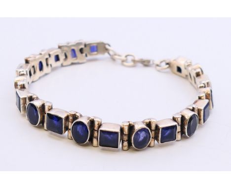 A silver articulated bracelet set with sapphire-coloured stones.  20 cm long. 