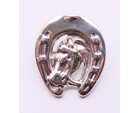 A silver brooch in the form of a horse's head within a horseshoe. 3 cm high.