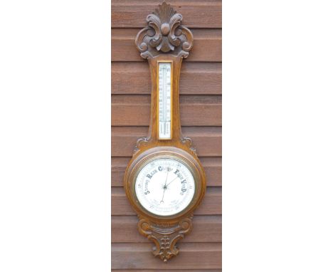 WHEEL BAROMETER WITH A WHITE DIAL ENCLOSING AN ANEROID MOVEMENT WITH A THERMOMETER, IN A CARVED OAK CASE (90.5 cm x 28.5 cm)