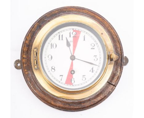 A brass and oak Radio Room bulkhead clock, the white enamel dial with Arabic numerals and red sectors at the 12 and 6 o'clock