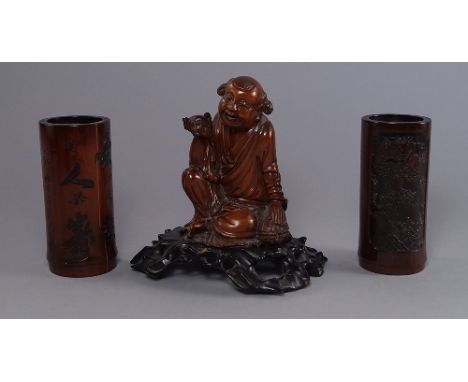 A Chinese hardwood carving of a young laughing man, late 19th/20th century, modelled holding a bat, seated his hand resting o