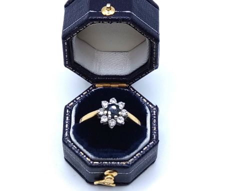 A yellow metal, sapphire, and diamond floral cluster ring, set with a dark blue round-cut sapphire within a border of round-c