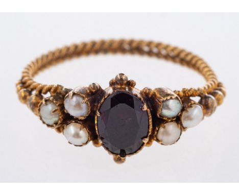 An antique closed back ring, set centrally with an oval-cut red stone (possibly garnet), each side set with a trefoil of seed