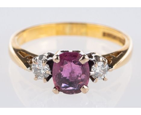 An 18ct yellow gold three stone ring, set to the centre with an oval-cut ruby with a pinkish hue and set each side with a bri