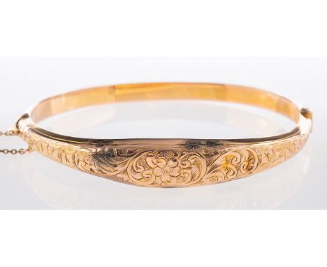 A 9ct yellow gold bangle, with flower and foliate engraving to the front section, (dented), hinged, safety chain, UK hallmark