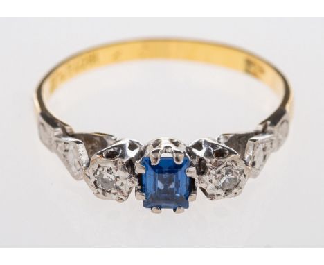 A three stone ring, set with a step-cut synthetic sapphire and set each side with a single-cut diamond, in an illusion settin