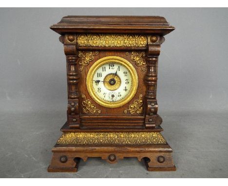 A Late 19th century oak-cased musical alarm clock, case having carved decoration and applied gilded mouldings, white enamel d