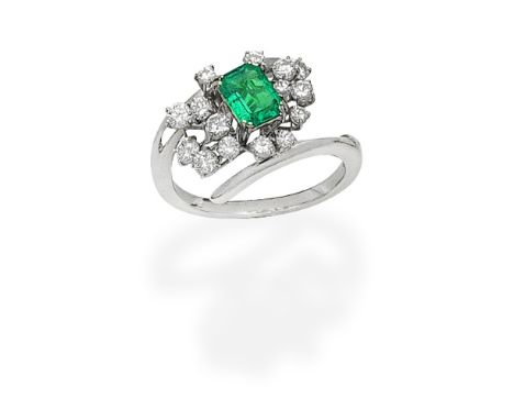 EMERALD AND DIAMOND DRESS RINGThe step-cut emerald within a spray of brilliant-cut diamonds, obliquely set between crossover 